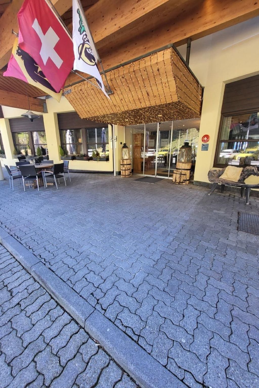 Ein Außenbereich mit Tischen, Stühlen, einer Holzpergola und Flaggen.