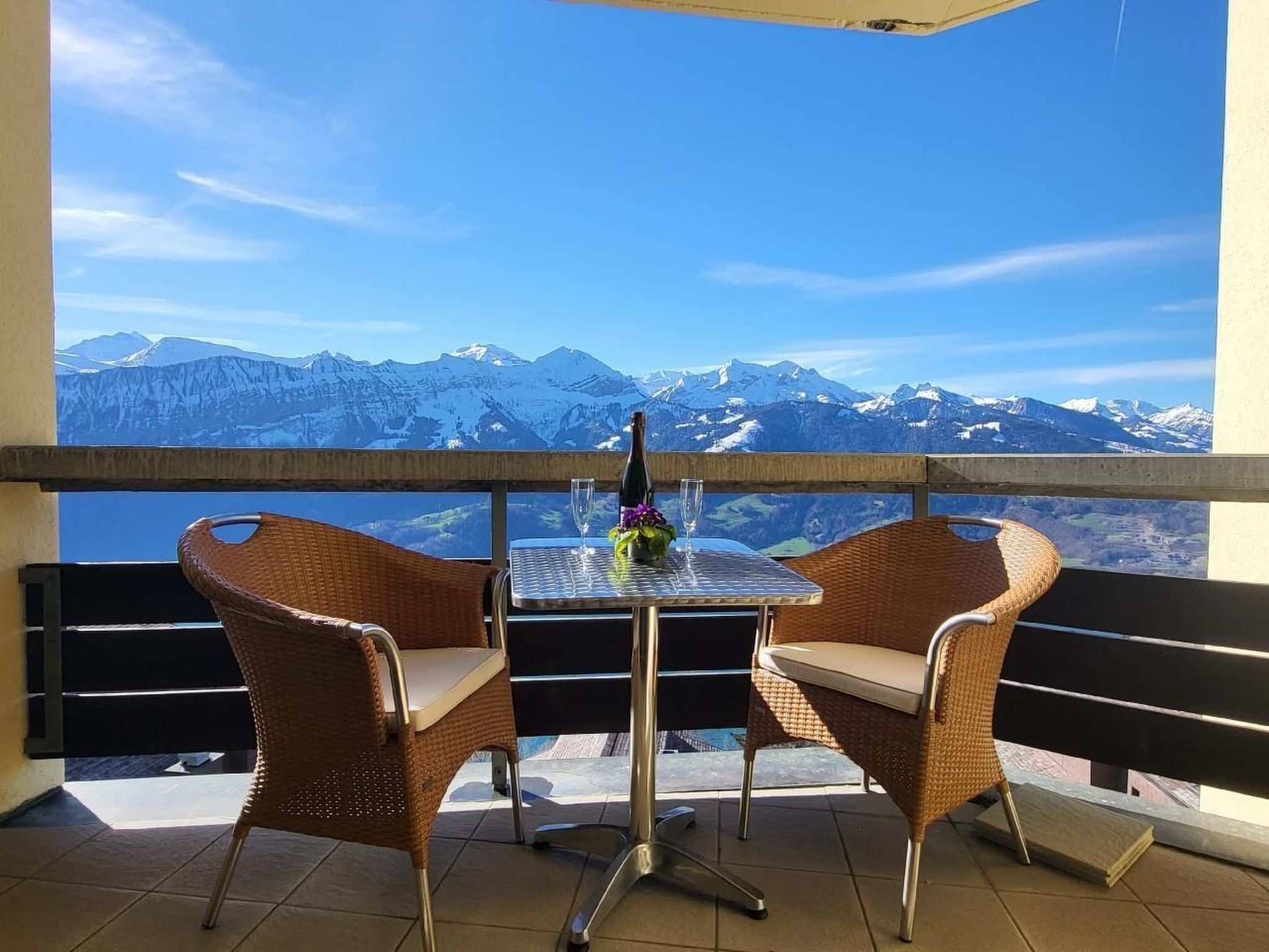 A balcony with wicker chairs and a table, overlooking a mountainous landscape.