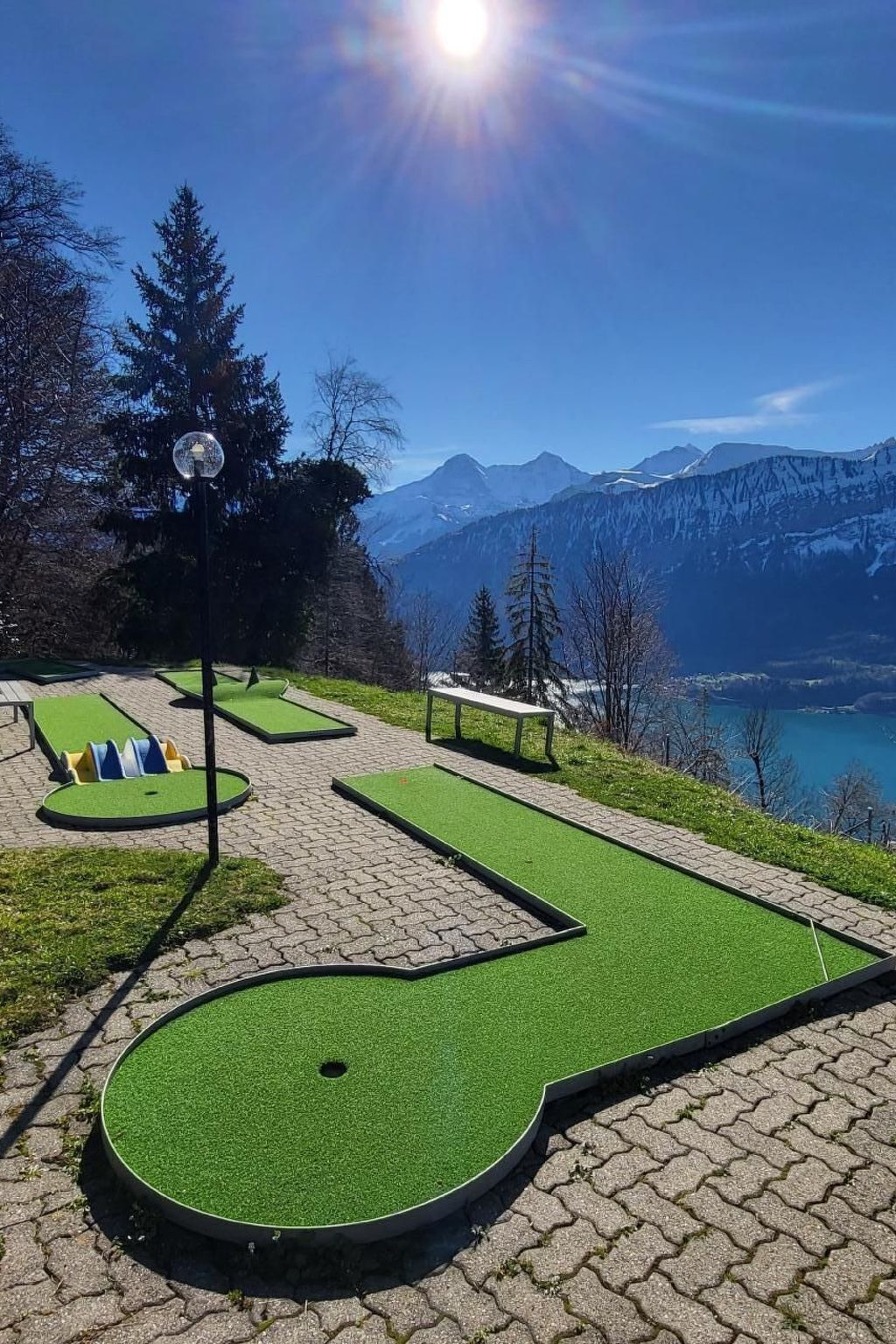 A miniature golf course with a scenic mountain view, a bench, and a lamp post.