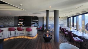 Et moderne barområde med en buet bar, røde barstole og en central pejs.