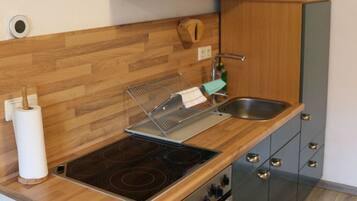 Cocina compacta con muebles de madera, pileta de acero inoxidable, horno empotrado y cocina.