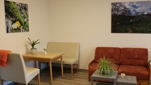 Ett vardagsrum med en beige soffa, ett träbord, ett litet bord med en växt och en tavla på väggen.