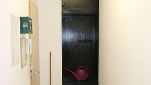 En smal hall med trägolv, en svart dörr med en röd vattenkokare ovanpå och en kvast som står lutad mot väggen.
