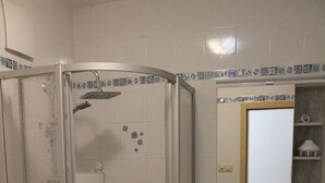 Ett badrum med en dusch som är avskärmad med glasväggar, ett handfat, en spegel och en handdukshängare.