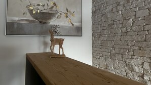 A room with a wooden table, a stone wall, and a painting of a still life with a bowl and branches. - Casa Ladina 4 by Interhome (Falera)