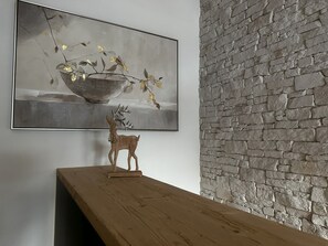 A room with a wooden table, a stone wall, and a painting of a still life with a bowl and branches. - Casa Ladina 4 by Interhome (Falera)