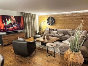 A modern living room with a flat-screen TV, wooden flooring, a sofa, a coffee table, and a decorative clock.