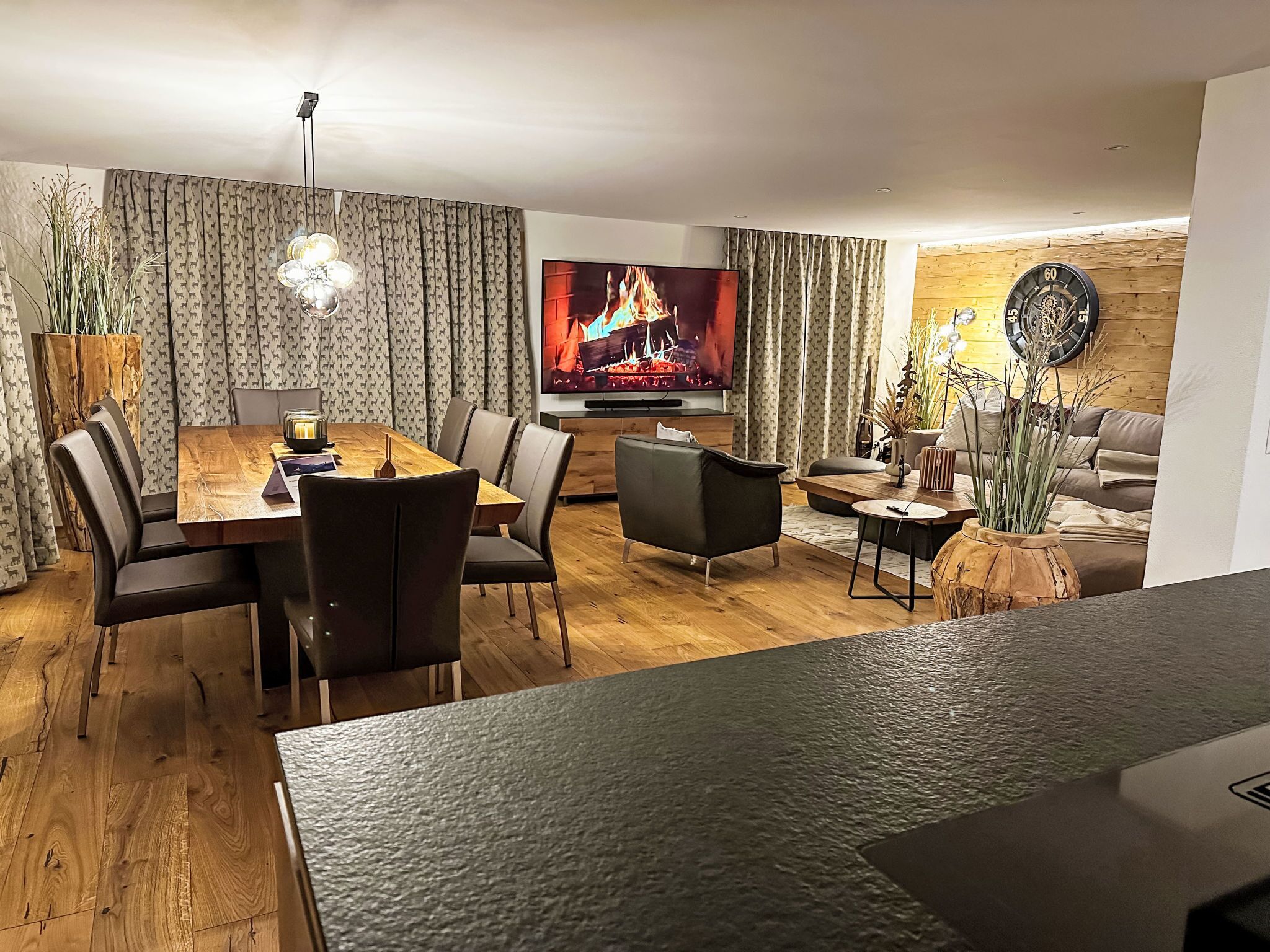 A modern living room with a flat-screen TV, wooden flooring, and a dining area with a table and chairs.