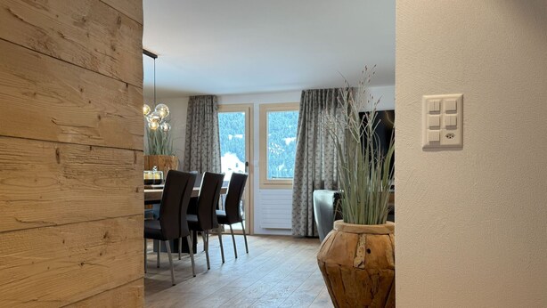 A modern dining area with a wooden floor, a dining table with chairs, and a large potted plant. - Casa Ladina 4 by Interhome (Falera)