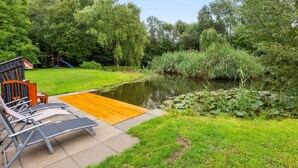 Ein ruhiger Außenbereich mit Holzterrasse, Liegestühlen und einem kleinen Teich, der von üppigem Grün umgeben ist.