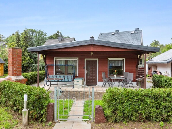 Ein rotes Holzhaus mit überdachter Terrasse, einer Bank und einem Tisch.