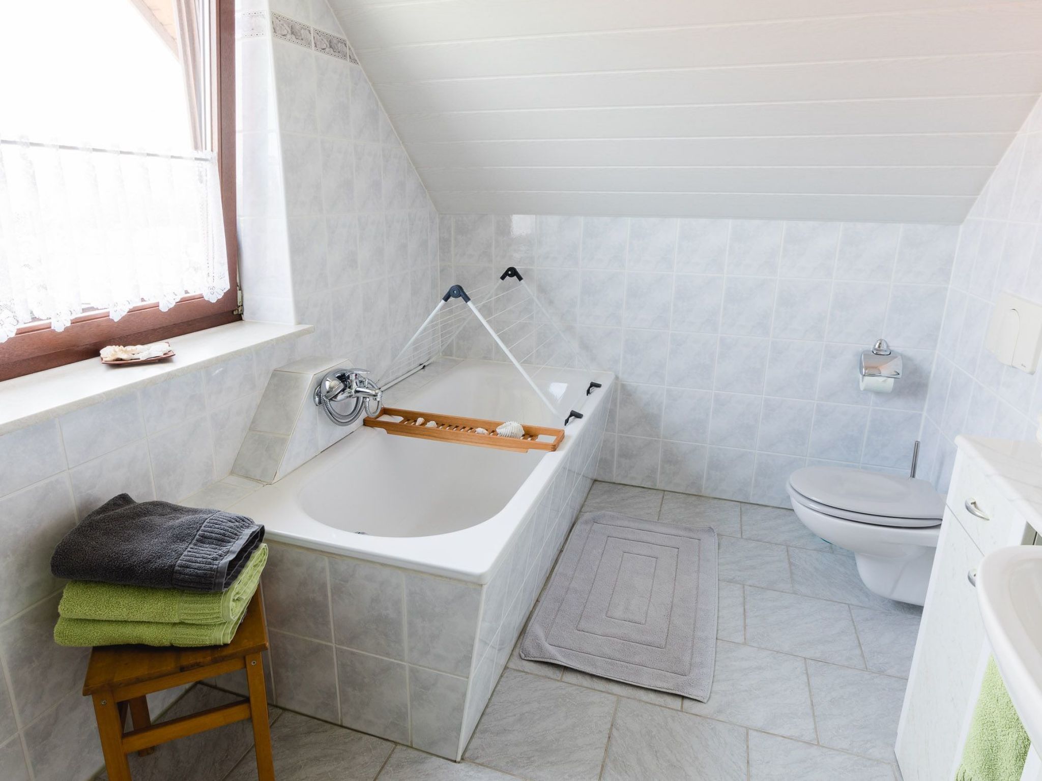 Une salle de bain avec une baignoire, des toilettes et une fenêtre ornée de rideaux en dentelle.