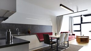 Una cuina moderna amb zona de menjador, una banca vermella amb coixins i un gran finestral amb cortines.