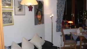 Ein gemütliches Wohnzimmer mit einem dunkelgrauen Sofa, einer Stehlampe und einem Essbereich mit Tisch und Stühlen.