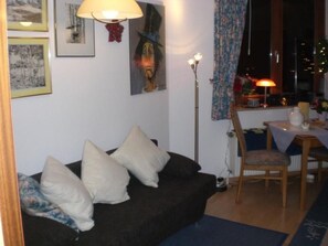 En hyggelig stue med en mørk sofa, en gulvlampe og et spiseområde med et bord og stole.