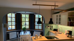 A kitchen with a central island, white cabinetry, a radiator, and large windows with a view of greenery. - Seerose by Interhome (Bleckede)