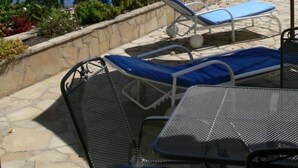 Un patio con un toldo a rayas, sillones de descanso y una sombrilla.