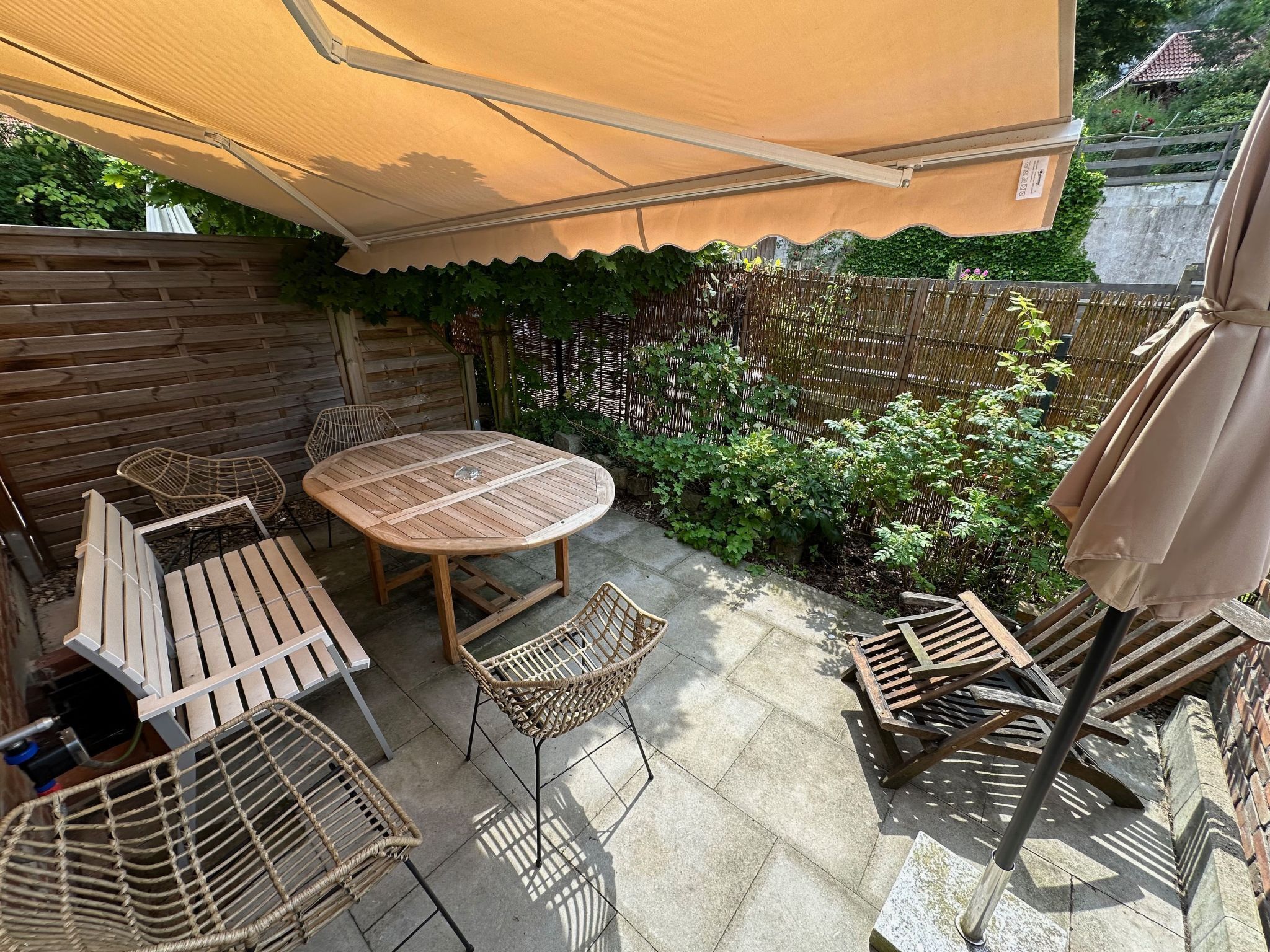 A patio with a round table and chairs, surrounded by a wooden fence and greenery.