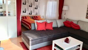 Un salon moderne avec un canapé gris, des coussins rouges, une table basse blanche et une bibliothèque.