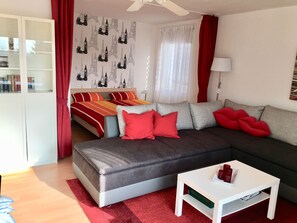 Ein modernes Wohnzimmer mit einem grauen Sofa, roten Kissen, einem weißen Couchtisch und einem Bücherregal.