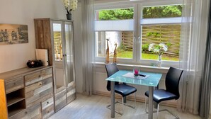 A modern dining area with a glass table and chairs, a wooden cabinet, and a view of the garden through large windows. - für zwei Personen, WLAN vorhanden by Interhome (Braunlage)