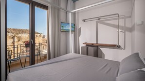 A hotel room with a bed, a TV on the wall, a balcony with chairs, and a view of the outside. - Guesthouse in the historic center - Bed 10.5 Design Suite (Castellammare del Golfo)
