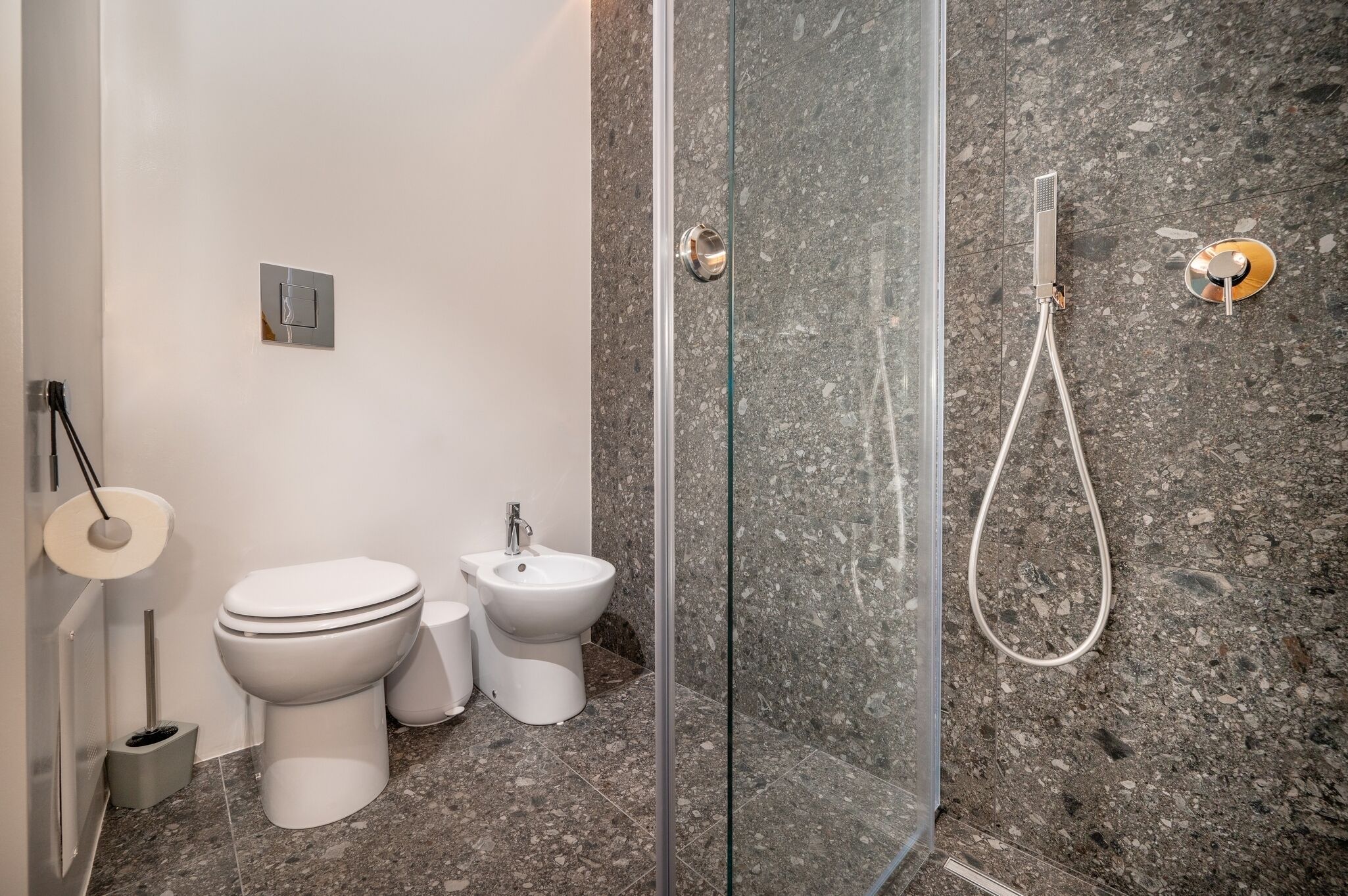 Een moderne badkamer met een douche met glazen wand, een toilet, een douchetoilet en een toiletbril.