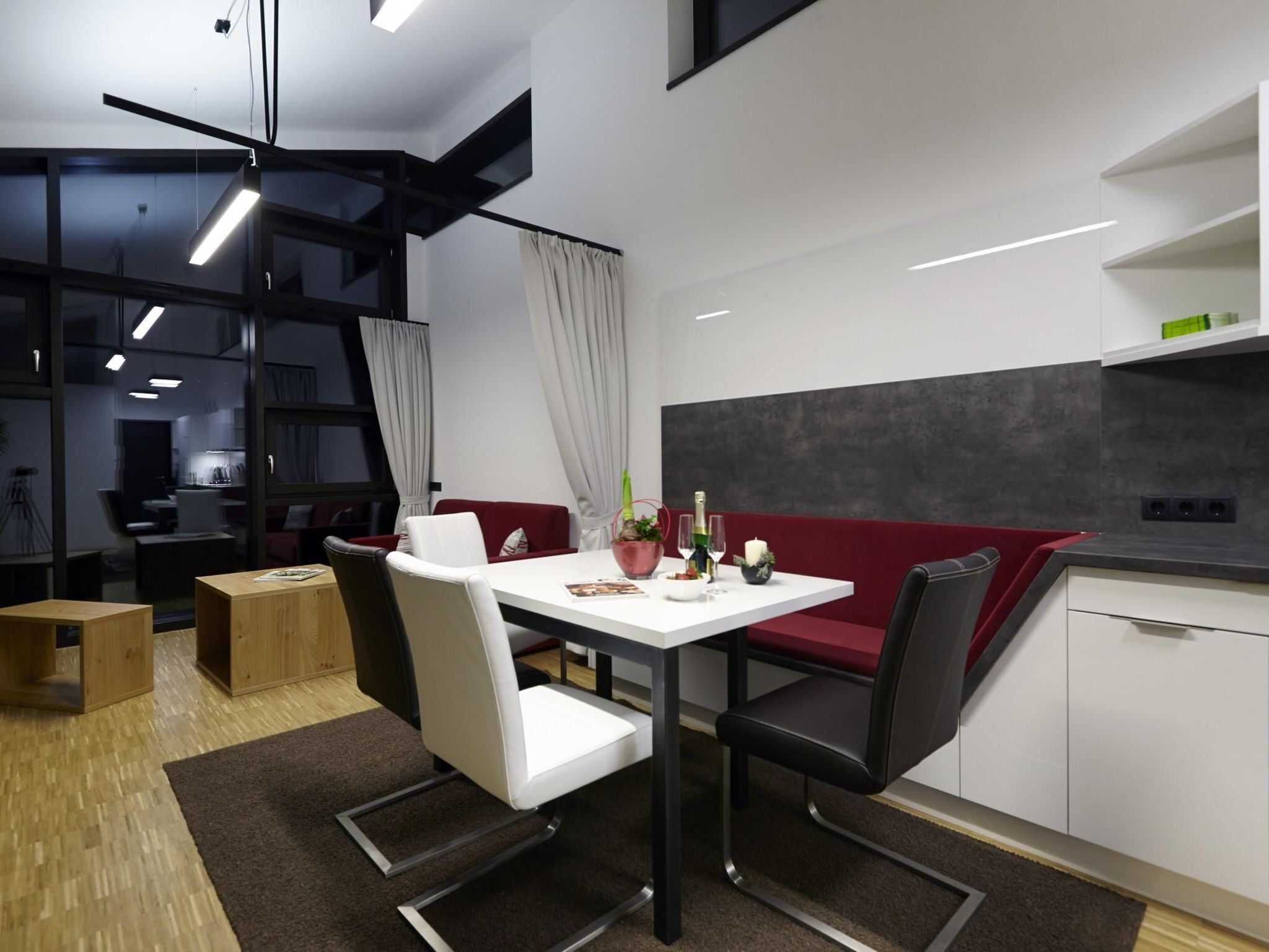 Een moderne keuken met witte kasten, een rode bank en een eettafel met stoelen.