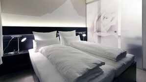 Et moderne hotelværelse med en stor seng, to sengeborde med lamper, en væg med rosedekoration og et stort vindue.