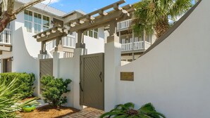 A gated entrance with a pergola, a small palm tree, and a plaque on the wall.