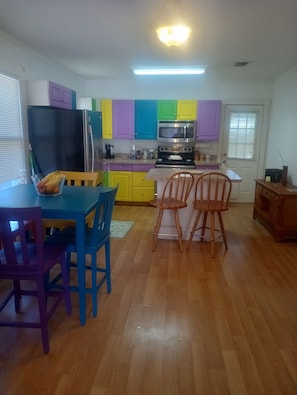 Une cuisine compacte avec des meubles de rangement aux couleurs vives, un réfrigérateur, un four à micro-ondes et un coin repas comprenant une table et des chaises.