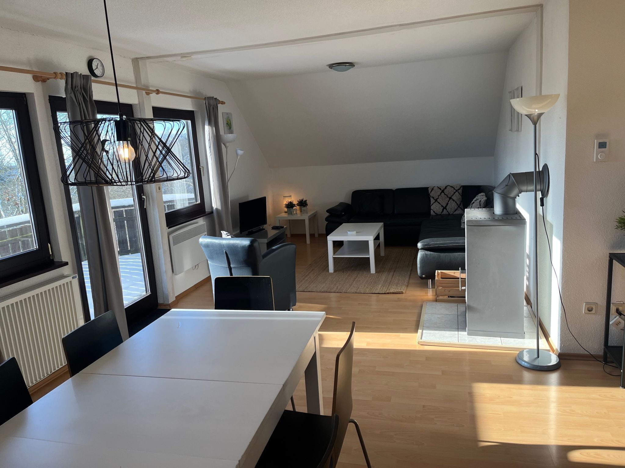 A modern living room with a white sofa, a black sofa, a dining table with chairs, a TV, and a lamp.