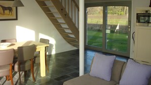 Ein Essbereich mit Holztisch und -stühlen, eine Treppe zu einem Balkon sowie Blick auf einen Garten.