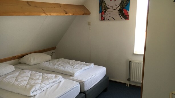 A room with two beds, a wooden ceiling beam, a radiator, and a painting on the wall. - für 6 Personen ca. 90 m² in Wemeldinge, Zeeland (Zuid-Beveland) by Interhome (Wemeldinge)