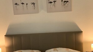 Een tweepersoonsbed met een bedsprei met dessin, een hoofdbord en twee aan de muur bevestigde afbeeldingen van vogels.