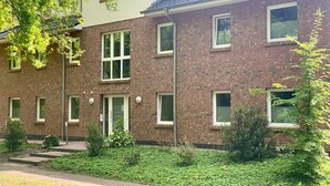 Een tweelaags bakstenen gebouw met veel ramen en een kleine tuin ervoor.