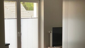 Een kamer met een schuifdeur naar een balkon, een donkere bank en een flatscreen televisie aan de wand bevestigd.