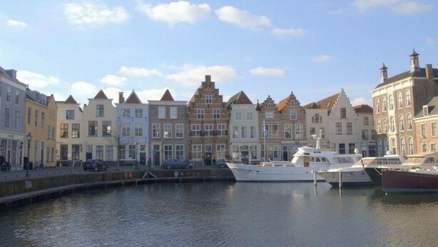 Vue sur un canal, avec une rangée de bâtiments européens traditionnels et un port de plaisance au premier plan.