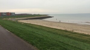 Une zone côtière comprenant une plage de sable, un champ d’herbe et un bâtiment doté de nombreuses fenêtres.
