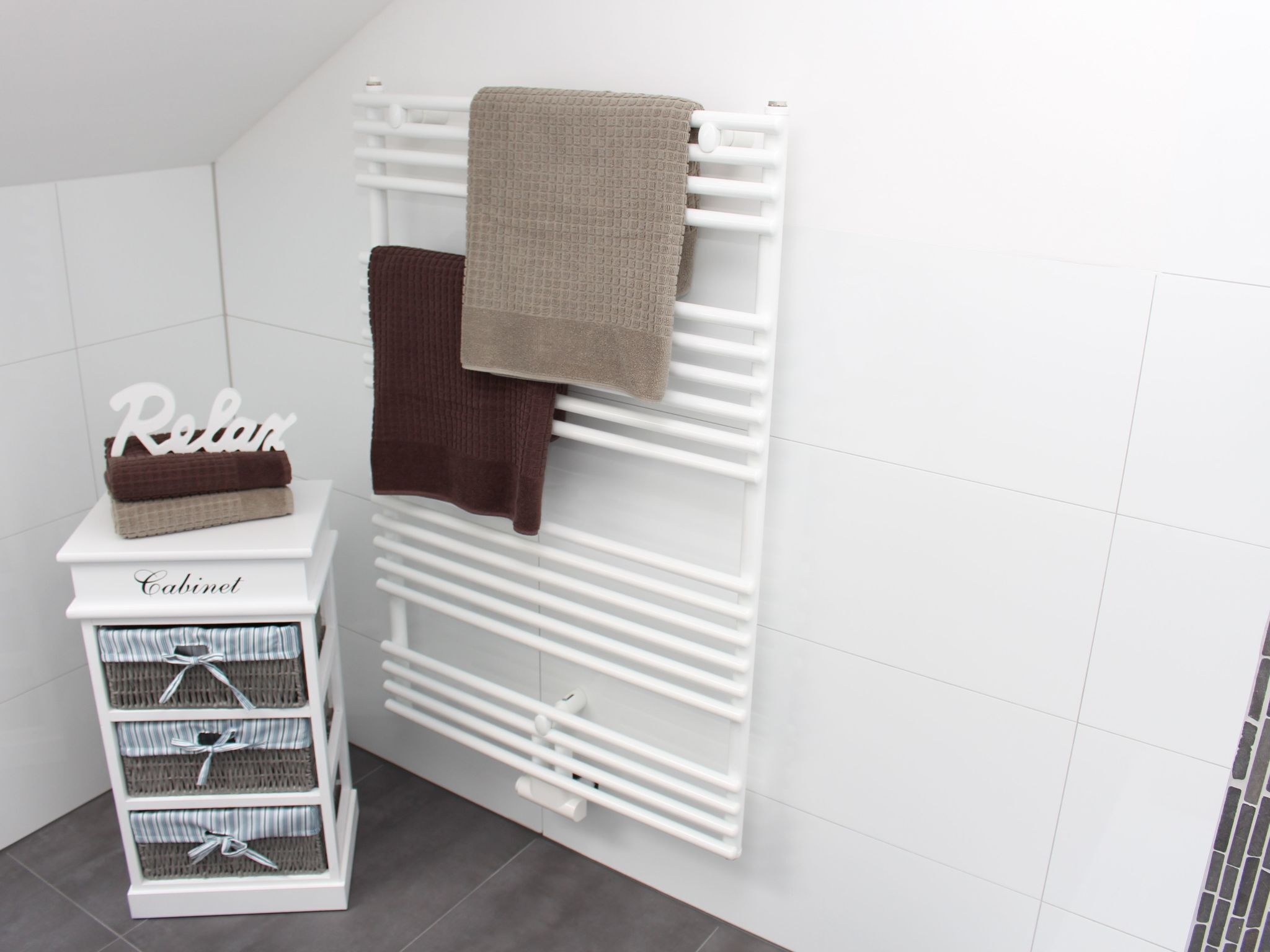 Ein weißer Schrank mit einem Schild mit der Aufschrift 'Relax' und einem Handtuchhalter mit Handtüchern.