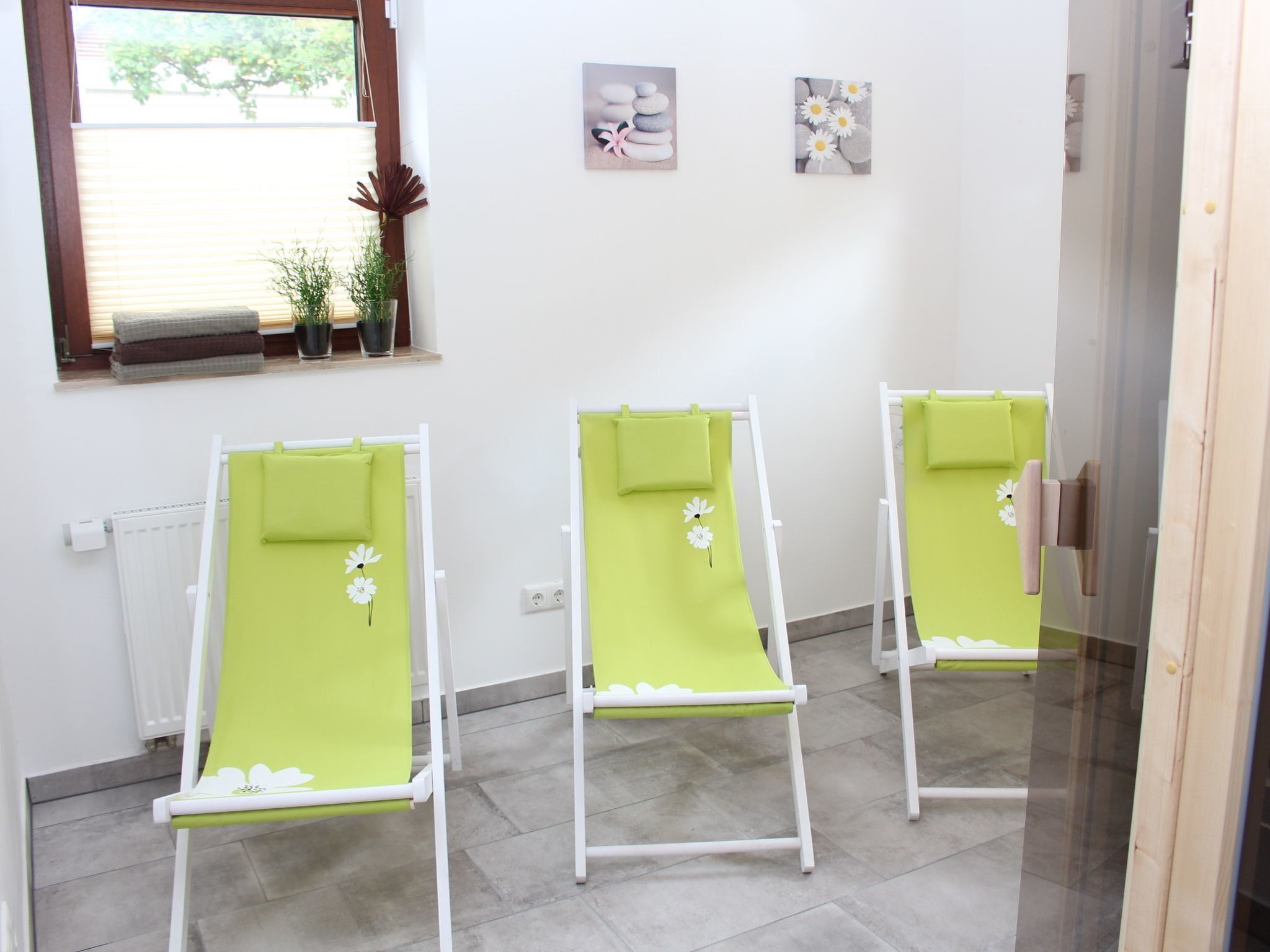 A room with three green massage chairs, a radiator, a window with blinds, and two small wall art pieces.