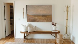 A room with a wooden bench, a large landscape painting, a coat stand, and a bookshelf. - NEW Boutique Historical Home Downtown Edmond (Edmond)