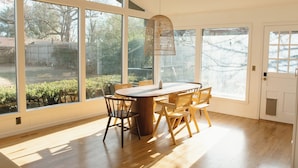 A dining area with a wooden table and chairs, large windows, and a hanging light fixture. - NEW Boutique Historical Home Downtown Edmond (Edmond)