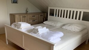 A bedroom with a white bed, wooden dresser, and a sloped ceiling. - mit Garten, Grill und Terrasse by Interhome (Julianadorp aan zee)