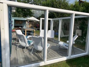 Une terrasse fermée par des baies vitrées, dotée de mobilier d’extérieur et offrant une vue sur le jardin arrière.