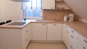 Een kleine keuken met een spoelbak, aanrecht, kastjes en een raam met jaloezieën.