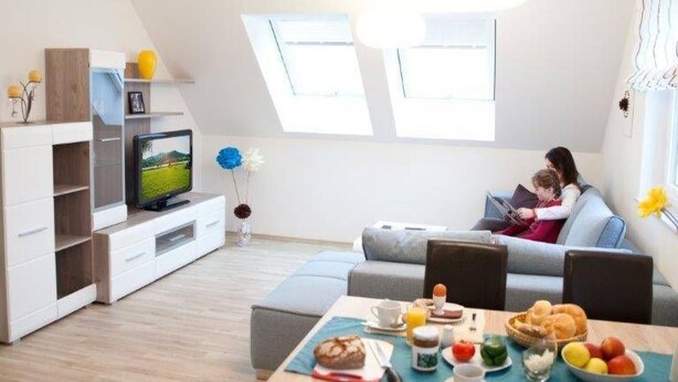 Een moderne woonkamer met een televisie, een eethoek met ontbijt, en een gezellige zithoek.