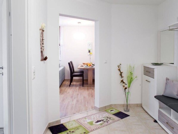 A hallway leading to a dining area with a table and chairs, a vase with dried plants, and a cabinet with a mirror.