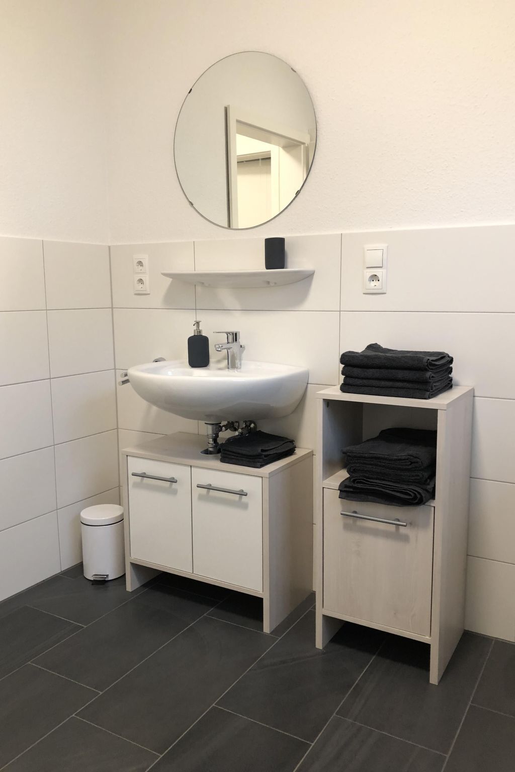 Et moderne badeværelse med en hvid vask, spejl og to skabe.
