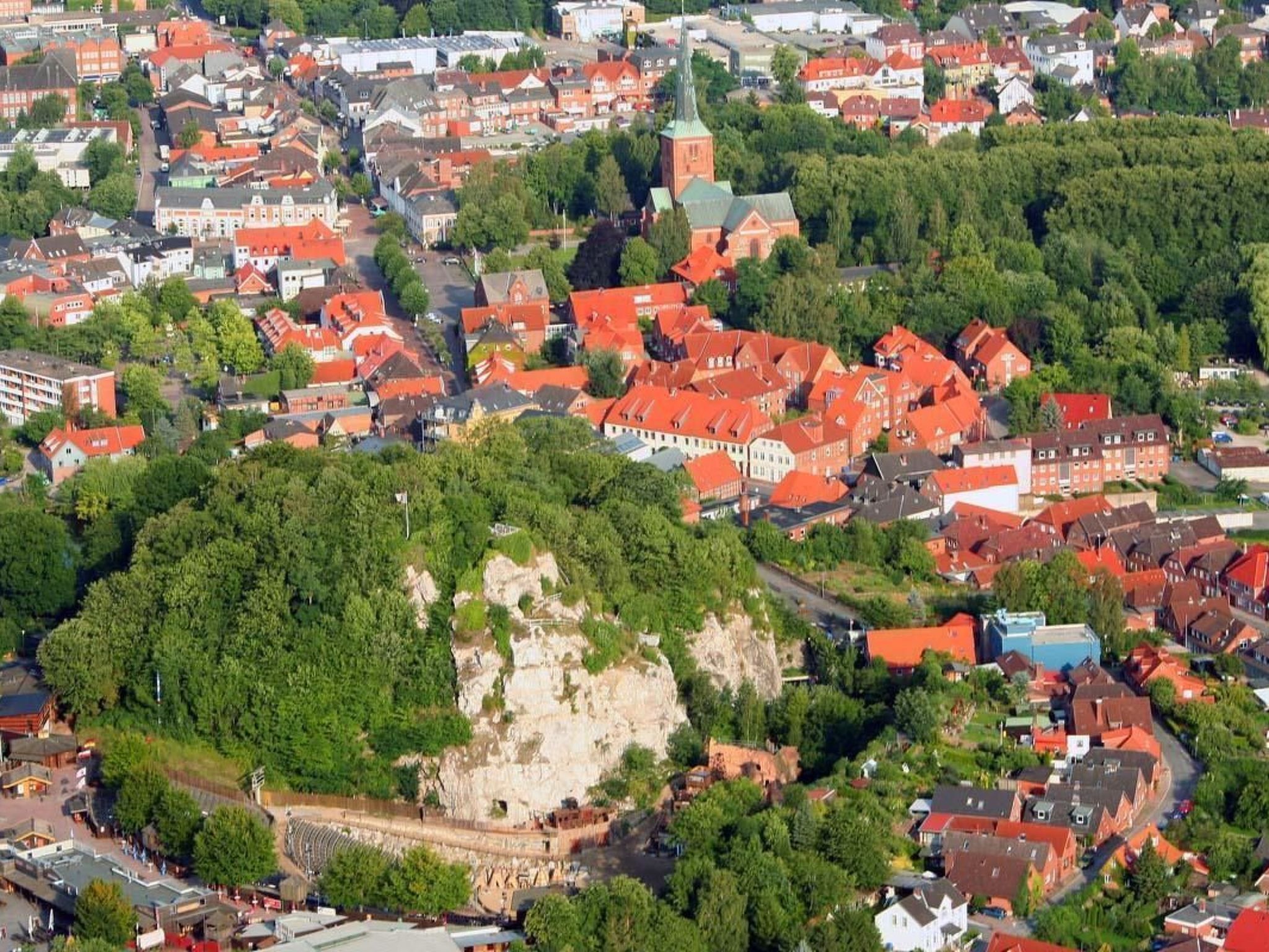 Luchtbeeld van een stad met rode daken, een opvallende kerk en een rotsheuvel met een fort.
